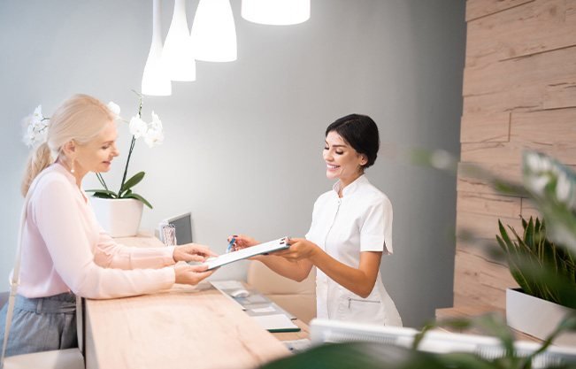 Smiling dental receptionist handing patient form