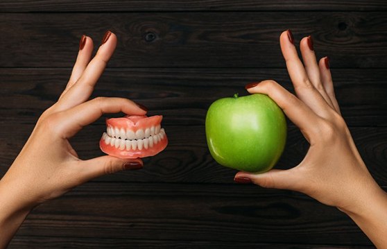 Close up of someone holding dentures and an apple